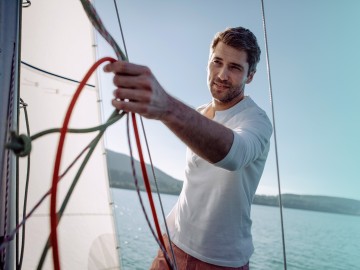Bootsversicherung: Junger Mann steuert Segelboot 