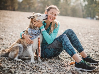 Hund sitzt neben einer Frau und schlecht diese im Gesicht ab