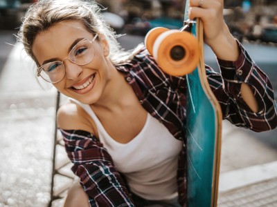 Zahn- & Brillenversicherung: Junge Frau lächelt und hält ein Skateboard fest