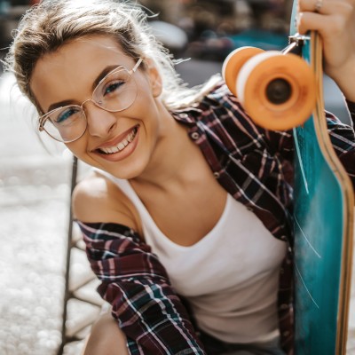 Zahn- & Brillenversicherung: Junge Frau lächelt und hält ein Skateboard fest