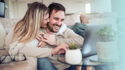 Junges Paar sitzt lachend und eng umschlungen vor einem Laptop