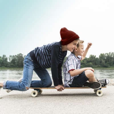 Kinderunfallversicherung: Zwei Jungs auf dem Skateboard am Flußufer