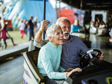 Versicherungen für Rentner & Senioren : Glückliches Seniorenpaar im Boxauto auf dem Jahrmarkt