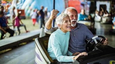 Unfallversicherung für Rentner & Senioren: Glückliches Seniorenpaar im Boxauto auf dem Jahrmarkt