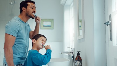 Vater und Sohn putzen sich vor dem Spiegel die Zähne