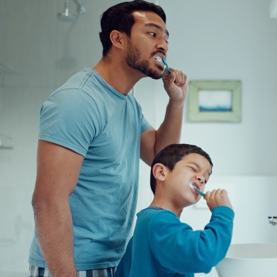 Vater und Sohn putzen sich vor dem Spiegel die Zähne