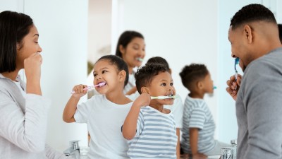 Eine Familie putzt sich gemeinsam vor dem Spiegel die Zähne.