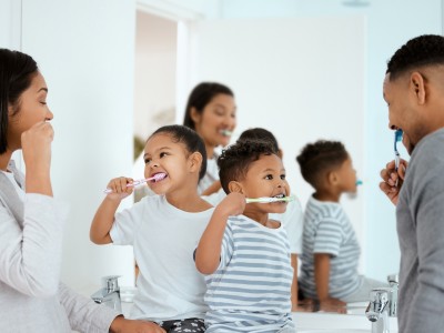 Eine Familie putzt sich gemeinsam vor dem Spiegel die Zähne.