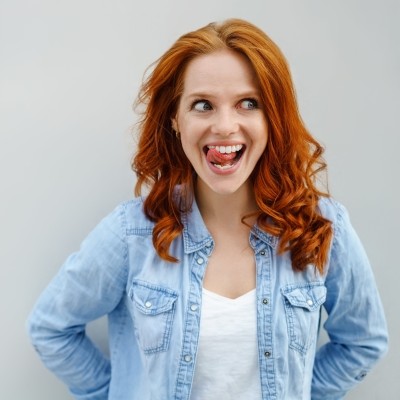Ist eine Zahnzusatzversicherung sinnvoll oder nicht?  : Rothaarige Frau streicht mit Ihrer Zunge über Ihre gepflegten Zähne