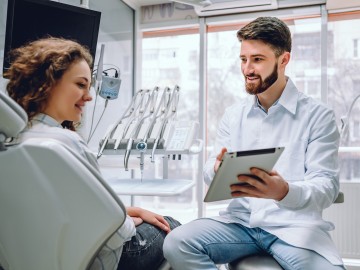 Ein Zahnarzt erklärt einer Patientin etwas auf einem Klemmbrett