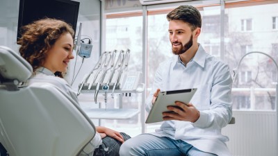 Ein Zahnarzt erklärt einer Patientin etwas auf einem Klemmbrett