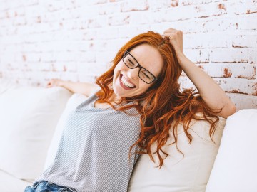 Eine Frau sitzt auf der Couch und lacht und zeigt dabei ihre weißen Zähne