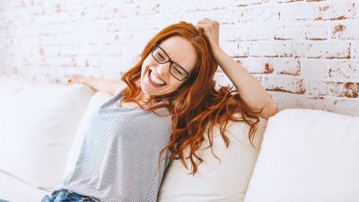 Eine Frau sitzt auf der Couch und lacht und zeigt dabei ihre weißen Zähne