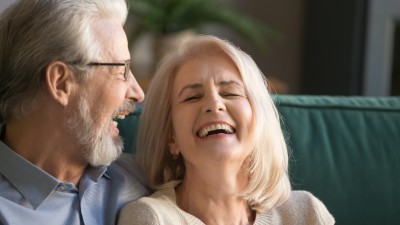 Zahnprothese - Arten, Kosten & Erstattung: Glückliches älteres Paar lachend auf dem Sofa