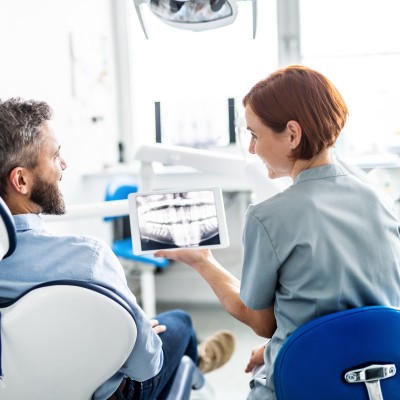 Die Zahn&auml;rztin zeigt dem Patienten ein R&ouml;ntgenbild auf dem Tablet