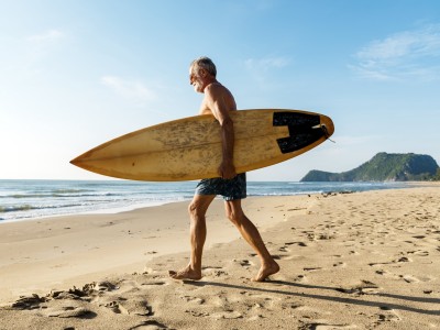 Senior mit dem Surfbrett am Strand