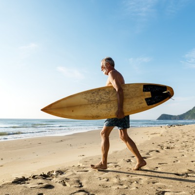 Senior mit dem Surfbrett am Strand