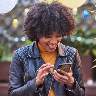 Frau mit Afrolook und mit Lederjacke bedient lächelnd Ihr Smartphone