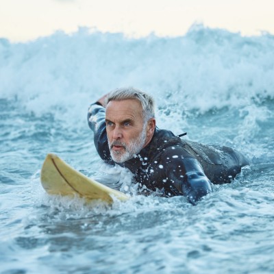 Unfallversicherung im Ausland  : Senior auf einem Surfboard in den Wellen