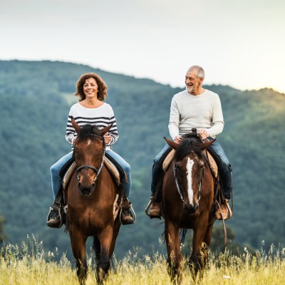 Unfallversicherung mit Beitragsrückgewähr: Paar mit zwei Pferden in der Natur unterwegs