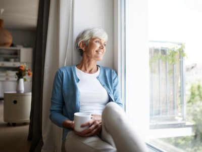 Seniorin schaut gemütlich auf einer Fensterbank sitzenden hinaus