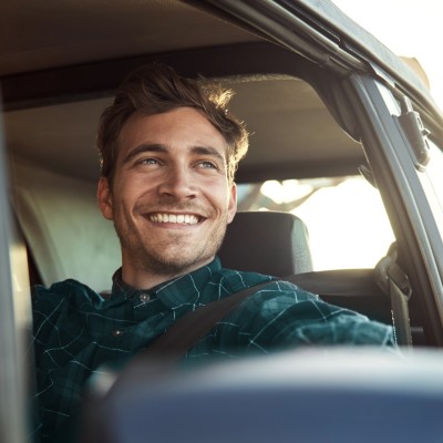 Fahrerschutzversicherung: Junger Mann schaut glücklich aus sein Auto