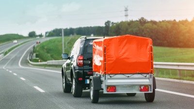 Anhänger-Versicherung: SUV mit kleinem Anhänger mit orangener Plane auf der Autobahn 