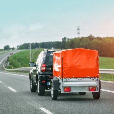 Anhänger-Versicherung: SUV mit kleinem Anhänger mit orangener Plane auf der Autobahn 