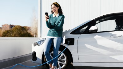 Elektroauto- & Hybrid-Versicherung: Junge Frau mit Ihrem Fahrzeug an der E-Ladestation