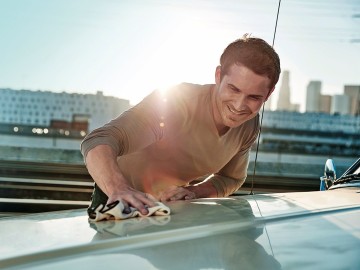 Ein Mann poliert die Motorhaube seines Autos.