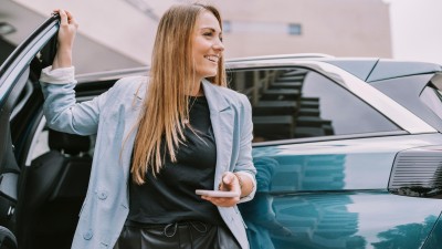 Auto ummelden : Frau mit Smartphone in der Hand lehnt an der Autotür