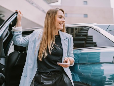 Auto ummelden : Frau mit Smartphone in der Hand lehnt an der Autotür