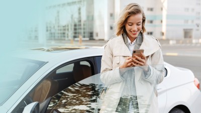 Frau mit Handy steht an der geöffneten Tür eines Autos