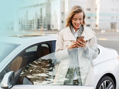 Frau mit Handy steht an der geöffneten Tür eines Autos