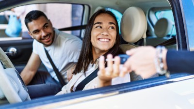 Zweitwagen versichern: Junge Fahrerin erhält Autoschlüssel durchs Seitenfenster gereicht