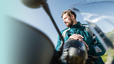 Motorradbekleidung-Versicherung: Motorradfahrer mit Lederjacke und Helm in der Hand