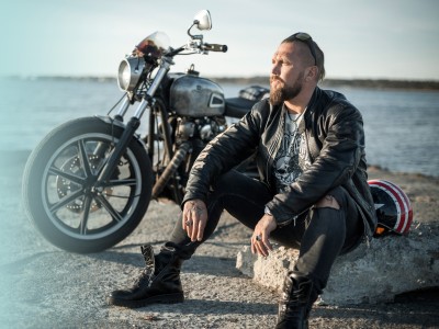 Motorradversicherung: Mann sitz vor seinem Motorrad am Wasser