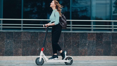 10 spannende Fakten über E-Scooter: Junge Frau fährt lachend auf EScooter die Straße entlang