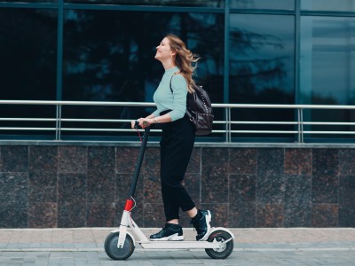 10 spannende Fakten über E-Scooter: Junge Frau fährt lachend auf EScooter die Straße entlang