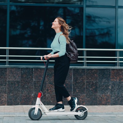 10 spannende Fakten über E-Scooter: Junge Frau fährt lachend auf EScooter die Straße entlang