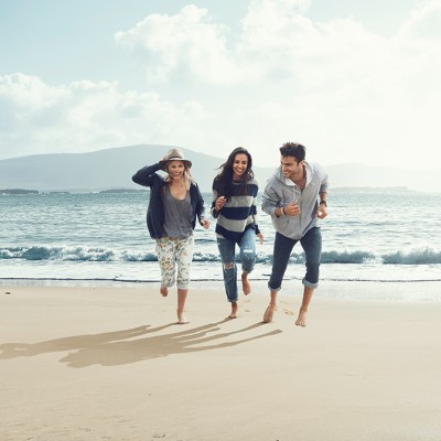 Hausratversicherung für Studenten: Drei junge Menschen sprinten an einem Strand