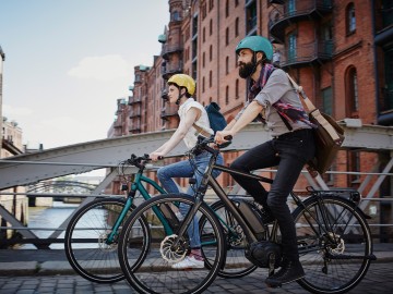 Fahrradversicherung: Zwei Menschen fahren mit ihren Farrädern über eine Brücke