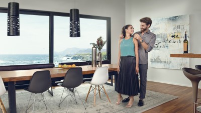 Hausratversicherung für Paare & Partner: Mann legt im Esszimmer Frau Halskette an, im Hintergrund, Küstenlandschaft