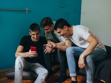 Drei junge Männer schauen gemeinsam auf ein Smartphone