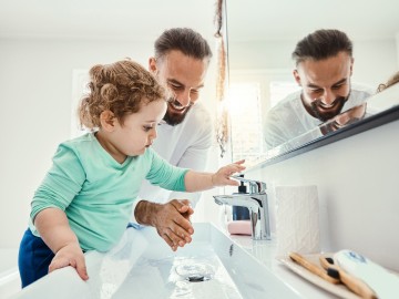 Vater und Kind am Waschbecken, das Kind macht das Wasser aus.