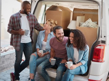 Vier junge Menschen trinken Kaffee hinter ihrem Transporter in dem Umzugskartons befinden.
