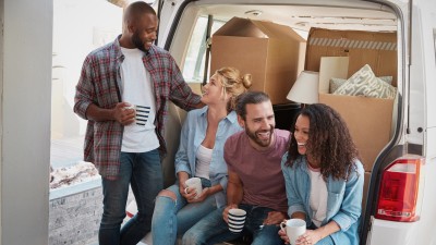 Vier junge Menschen trinken Kaffee hinter ihrem Transporter in dem Umzugskartons befinden.