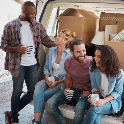 Vier junge Menschen trinken Kaffee hinter ihrem Transporter in dem Umzugskartons befinden.