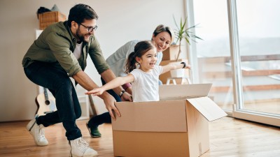 Die Eltern spielen mit ihrer Tochter, die in einem Umzugskarton sitzt.