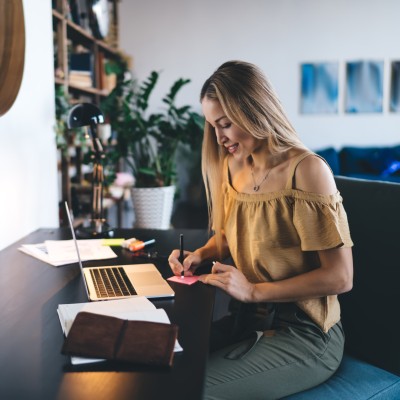 Frau sitzt am offenen Laptop und schreibt dazu einen Post-it